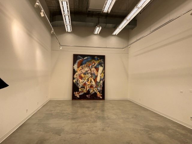 A modern art gallery room with blank white walls, polished concrete floors, and a colorful abstract painting mounted on the far wall under bright ceiling lights.