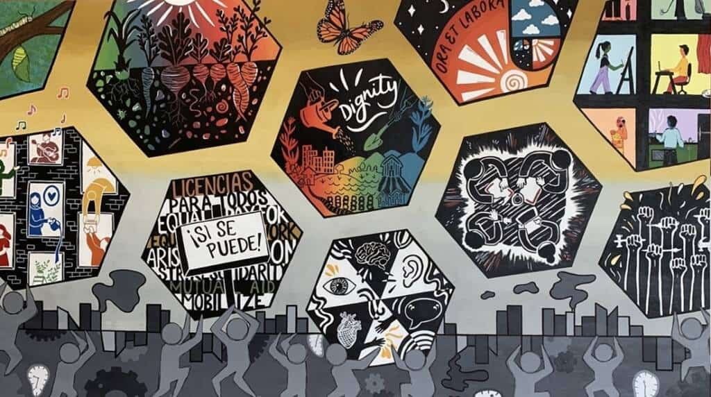 A colorful mural features hexagonal panels depicting themes of unity, justice, dignity, and empowerment. Below, gray silhouettes of people stand against an abstract cityscape background.