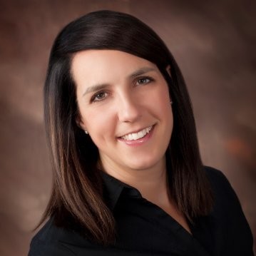 Professional headshot of a woman with straight, dark brown hair, wearing a black shirt and smiling at the camera against a softly blurred brown background.