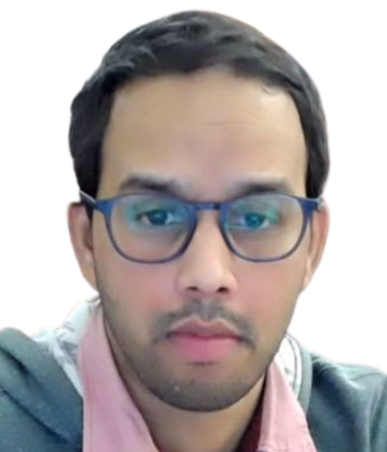 A person with short dark hair and glasses is looking directly at the camera. They are wearing a pink collared shirt under a gray hoodie. The background is white.