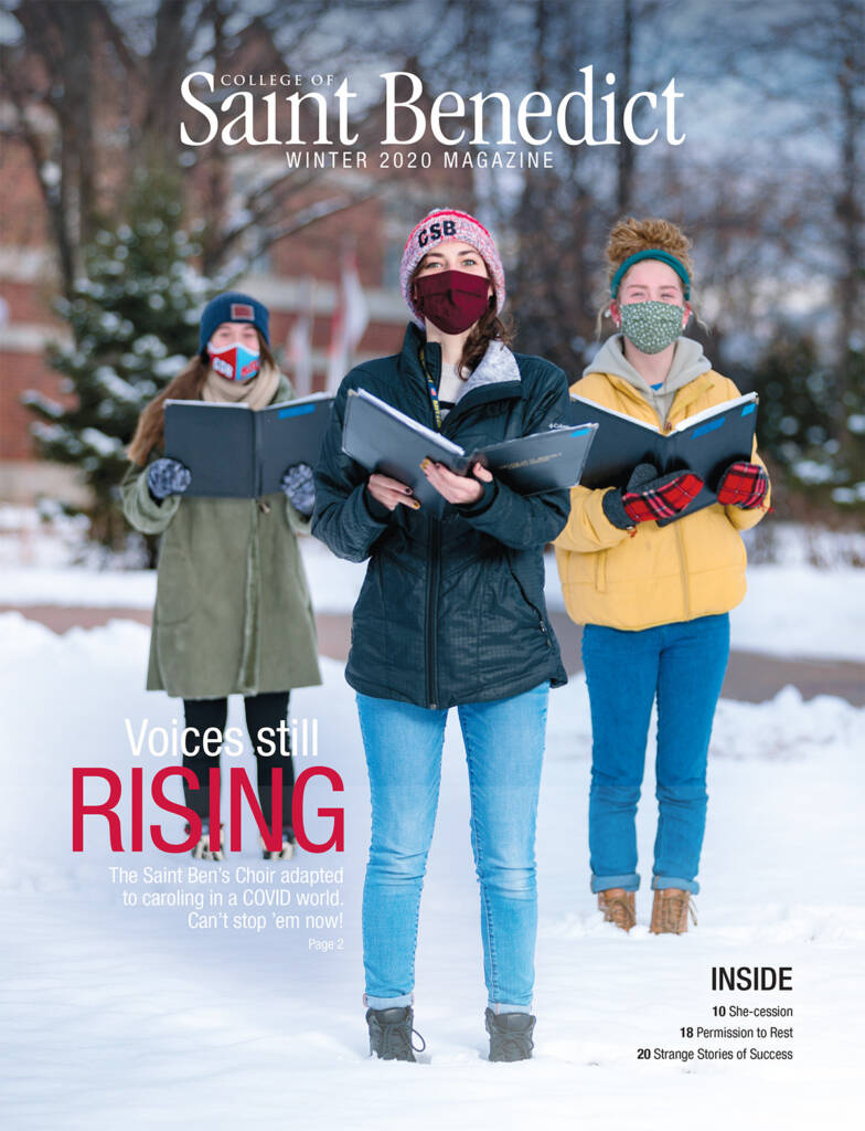 Three people wearing masks and winter clothing stand outdoors in the snow, holding music binders. The cover text reads, "Voices still rising. The Saint Ben's Choir adapted to caroling in a COVID world. Can't stop 'em now!.