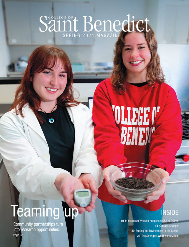 Two smiling women stand in a lab. One wears a lab coat and holds a small device; the other wears a red "College of Saint Benedict" sweatshirt and holds a bowl with seeds. The text reads "College of Saint Benedict Spring 2024 Magazine" and "Teaming up.