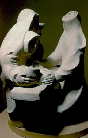 Abstract stone sculpture of three figures in flowing robes, two holding and supporting a third reclining figure. The expressions and poses evoke a sense of grief, compassion, and support.