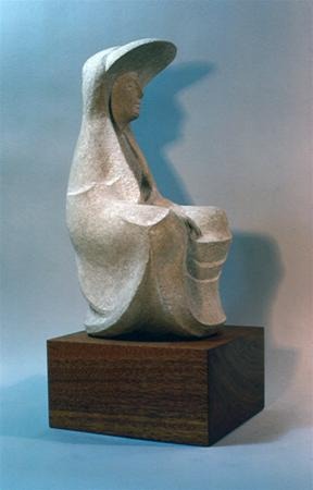 A stone sculpture of a seated figure wearing a draped robe and a large, rounded hat, mounted on a wooden base. The figure's features are smooth and stylized, with a contemplative expression.