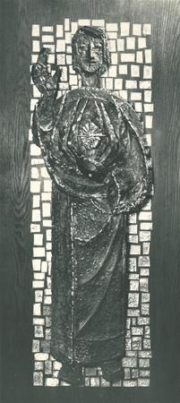 Black and white image of a relief sculpture depicting a standing figure in long robes, with one hand raised in blessing and a radiant heart on the chest, set against a background of small square tiles.