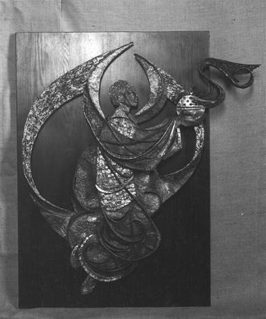 Black and white image of a relief sculpture showing a robed, winged figure holding a lamp, mounted on a wooden panel. The figure appears to be in motion, with flowing garments and dynamic curved shapes.