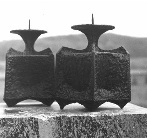Two large, textured metal objects with pointed tops sit side by side on a stone surface outdoors, with blurry hills visible in the background.