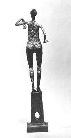 A rough-textured, elongated bronze sculpture of a standing human figure seen from behind, with one arm bent upward and the other extended, mounted on a rectangular base with a circular hole.