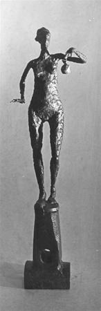 A tall, slender bronze sculpture of a simplified human figure stands on a rectangular base. The figure holds a small object in its raised right hand and has rough, textured surfaces. The background is plain.