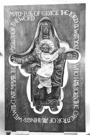 A carved wooden icon of Mary holding the infant Jesus, with an inscription encircling them that reads: "Mary full of grace the Lord is with you who has borne the creator of all things we will contemplate the mystery of the word.