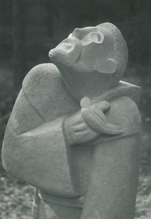 A stone sculpture of a bearded man looking upward, with a small bird perched on his hand. The figure appears peaceful and contemplative, wearing simple robes.
