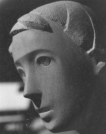 Black and white close-up photo of a smooth stone sculpture depicting a human face with stylized features, gazing slightly downward with calm, contemplative expression.
