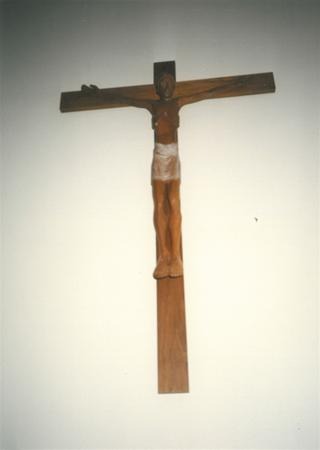 A wooden crucifix featuring a carved figure of Jesus with arms outstretched, wearing a cloth around the waist, mounted on a plain wall.