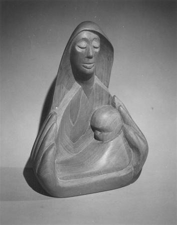 Wooden sculpture of a woman with closed eyes, holding an infant in her arms, carved in smooth, flowing lines. The scene suggests tenderness and maternal care. The background is plain and softly lit.