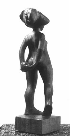A wooden sculpture of a standing nude human figure with an animal-like head, holding an object behind its back, displayed on a rectangular base against a plain background.