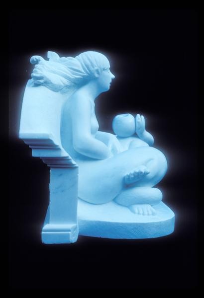 A blue-tinted sculpture of a seated woman with long flowing hair, sitting cross-legged and holding a child in her lap, both facing to the right, with part of a bench or structure behind her.