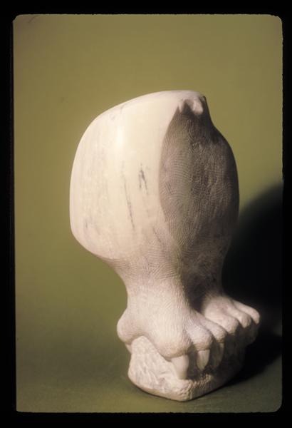 A smooth, abstract white sculpture resembling an owl with minimal features, perched on a textured base, is displayed against a plain olive-green background.