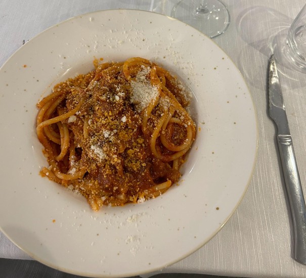 A plate of spaghetti topped with red sauce and sprinkled with grated cheese. The plate is set on a white tablecloth, accompanied by a knife and a wine glass.