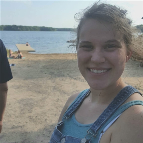 Girl in overalls smiling on the shore of a lake