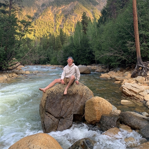 Guy sitting on a rock on the edge of a river 
