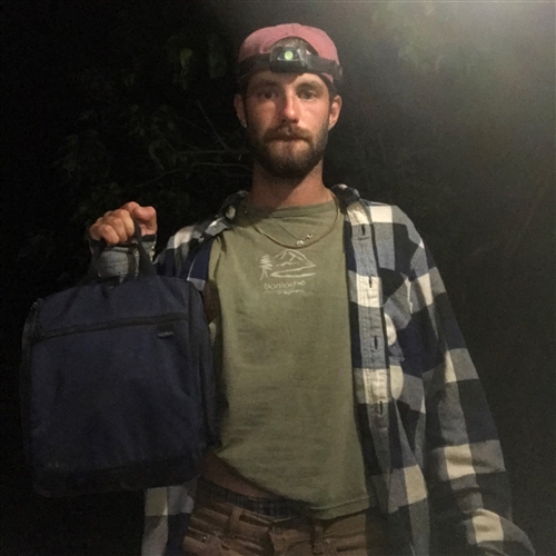 Guy in flannel shirt in the dark holding a bag