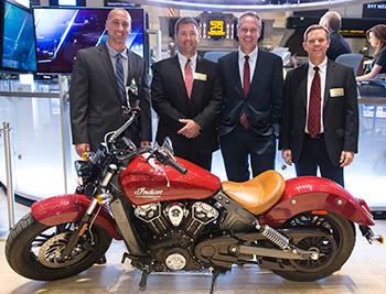 Photo of the four Johnnie alums with an Indian Scout motorcycle on the floor of the NYSE