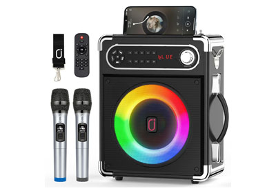 Portable karaoke machine with a rainbow LED speaker, two wireless microphones, a remote control, a black strap, and a smartphone placed on top of the speaker.