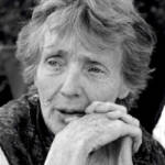 Elderly person with short, wispy hair, resting their chin on clasped hands, gazing thoughtfully. The image is in black and white, capturing detailed facial expressions and textures.