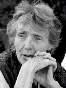 Elderly person with short, wispy hair, resting their chin on clasped hands, gazing thoughtfully. The image is in black and white, capturing detailed facial expressions and textures.