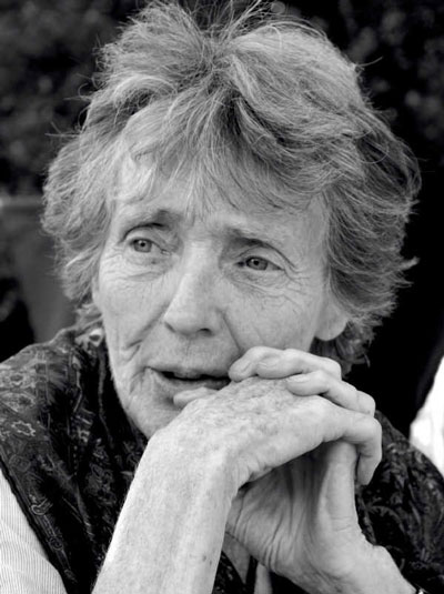 Elderly person with short, wispy hair, resting their chin on clasped hands, gazing thoughtfully. The image is in black and white, capturing detailed facial expressions and textures.