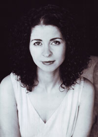 A black and white portrait of a person with curly hair, wearing a light-colored sleeveless top. They are seated and looking directly at the camera with a neutral expression.