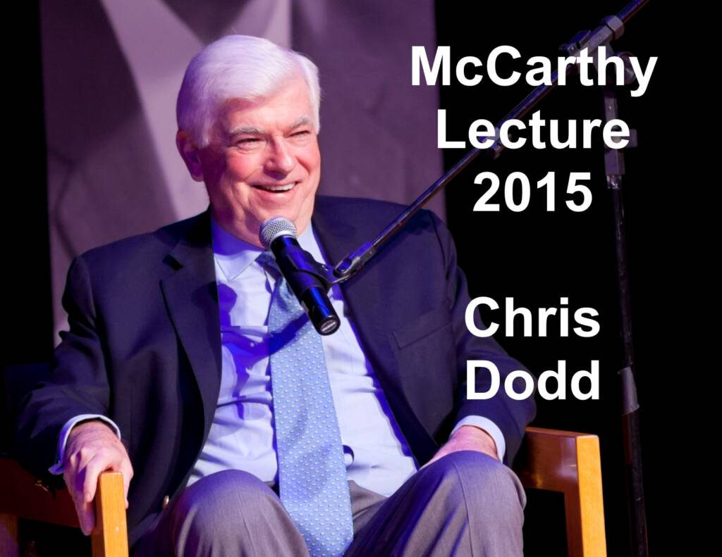 A man with white hair in a dark suit and blue tie smiles while speaking into a microphone. He is seated on a wooden chair. The text on the image reads, "McCarthy Lecture 2015 Chris Dodd.