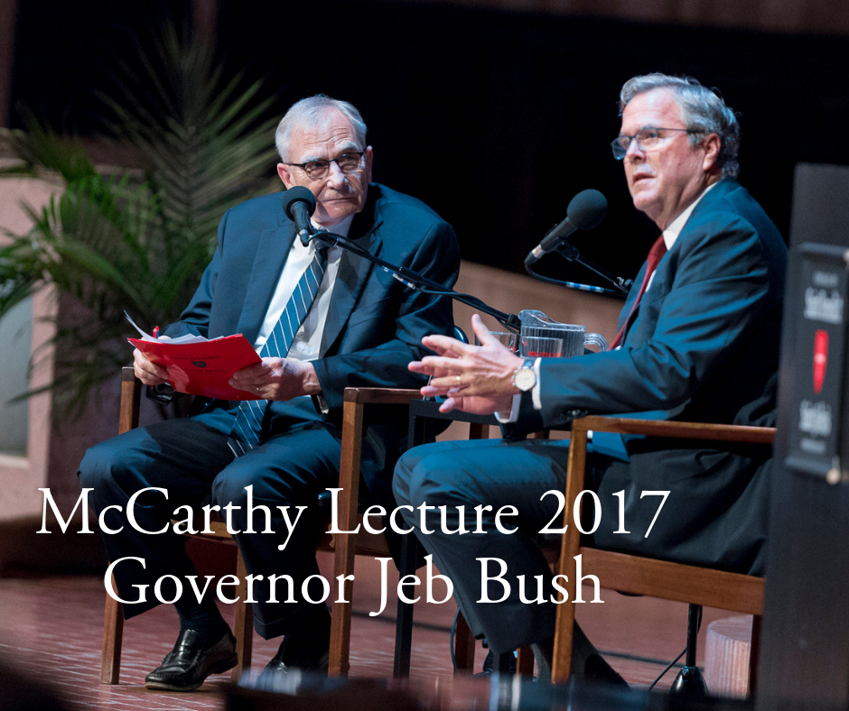 Two men are seated on stage with microphones, engaged in conversation during the McCarthy Lecture 2017. The man on the right is gesturing with his hands while speaking. The text in the foreground reads, "McCarthy Lecture 2017 Governor Jeb Bush.