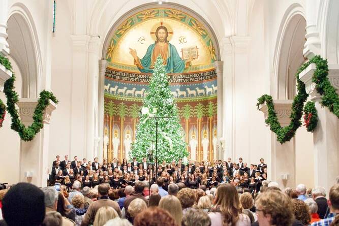 A large choir performs in front of a decorated Christmas tree inside a church adorned with festive garlands, with a congregation seated and standing, and a mural of Jesus above the altar.