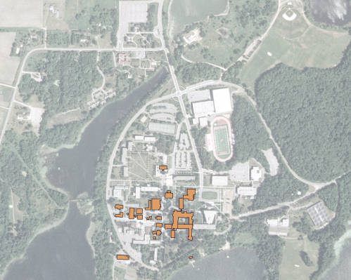 Aerial view of a large campus surrounded by greenery and water bodies. Buildings are highlighted in orange, and a stadium is visible. Roads and paths connect different parts of the area, providing a clear layout of the facilities.