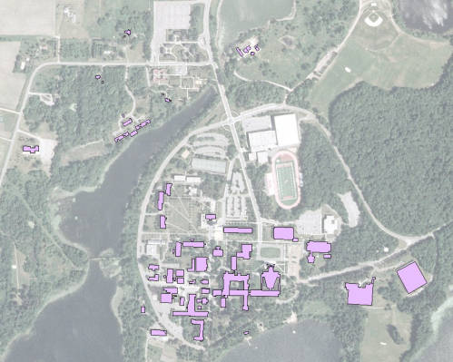 Aerial view of a campus map with buildings highlighted in purple. The image includes roads, trees, bodies of water, and a sports field with a running track. The campus appears to be surrounded by greenery.