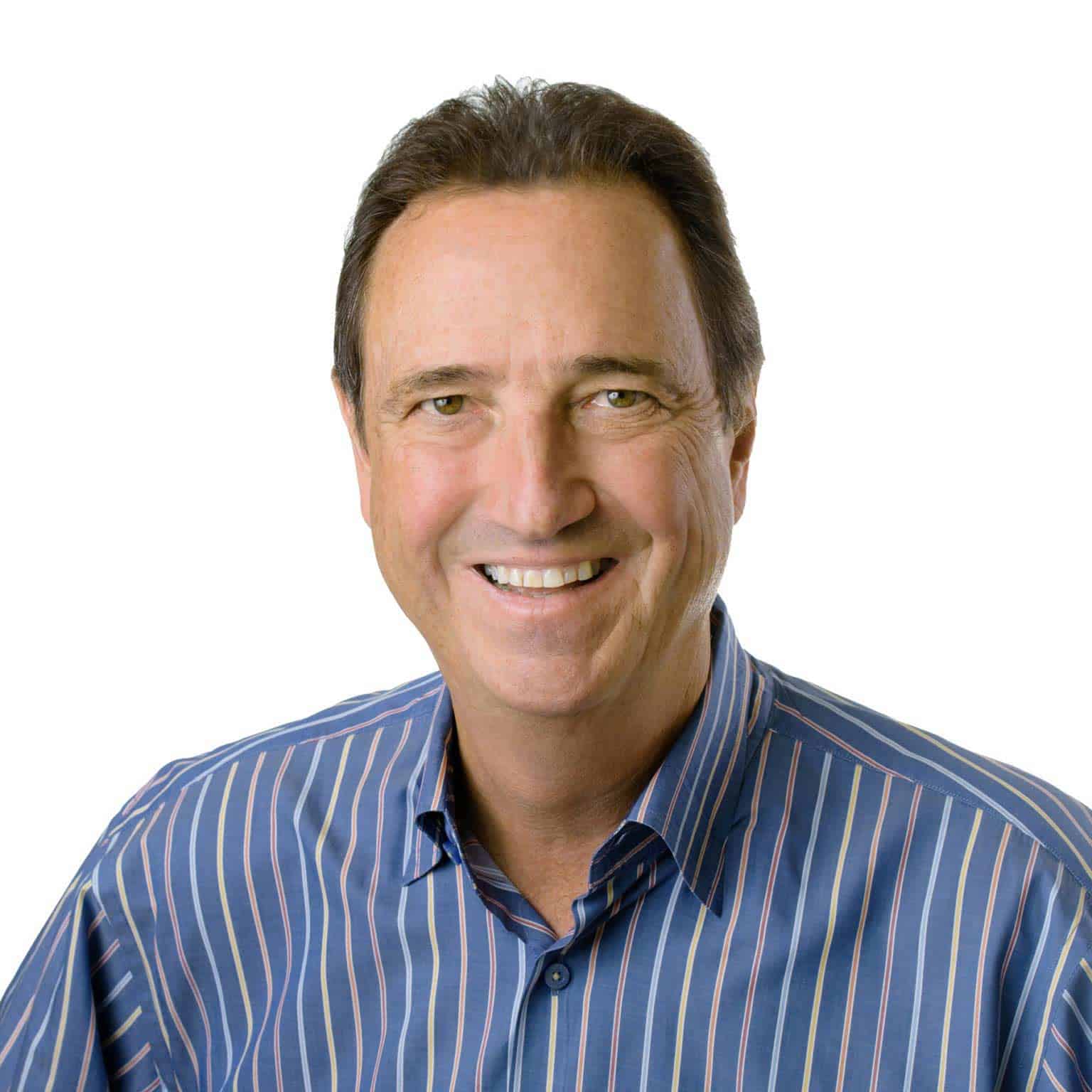 A middle-aged man with short dark hair smiles at the camera. He is wearing a blue striped button-up shirt and is posed against a plain white background.