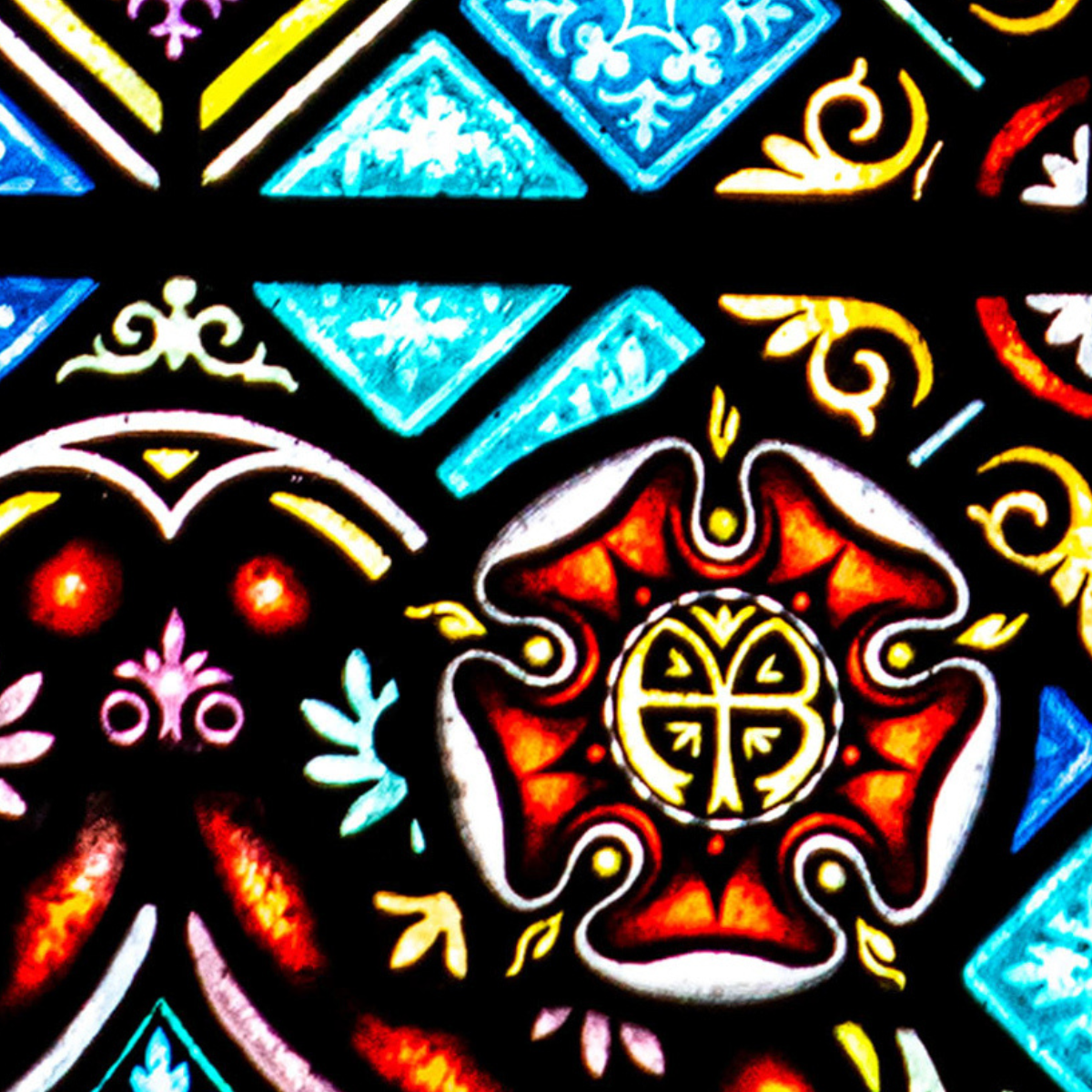 Colorful stained glass featuring geometric shapes, ornate patterns, and a central red and yellow floral design, with blue and aqua diamonds in the background.
