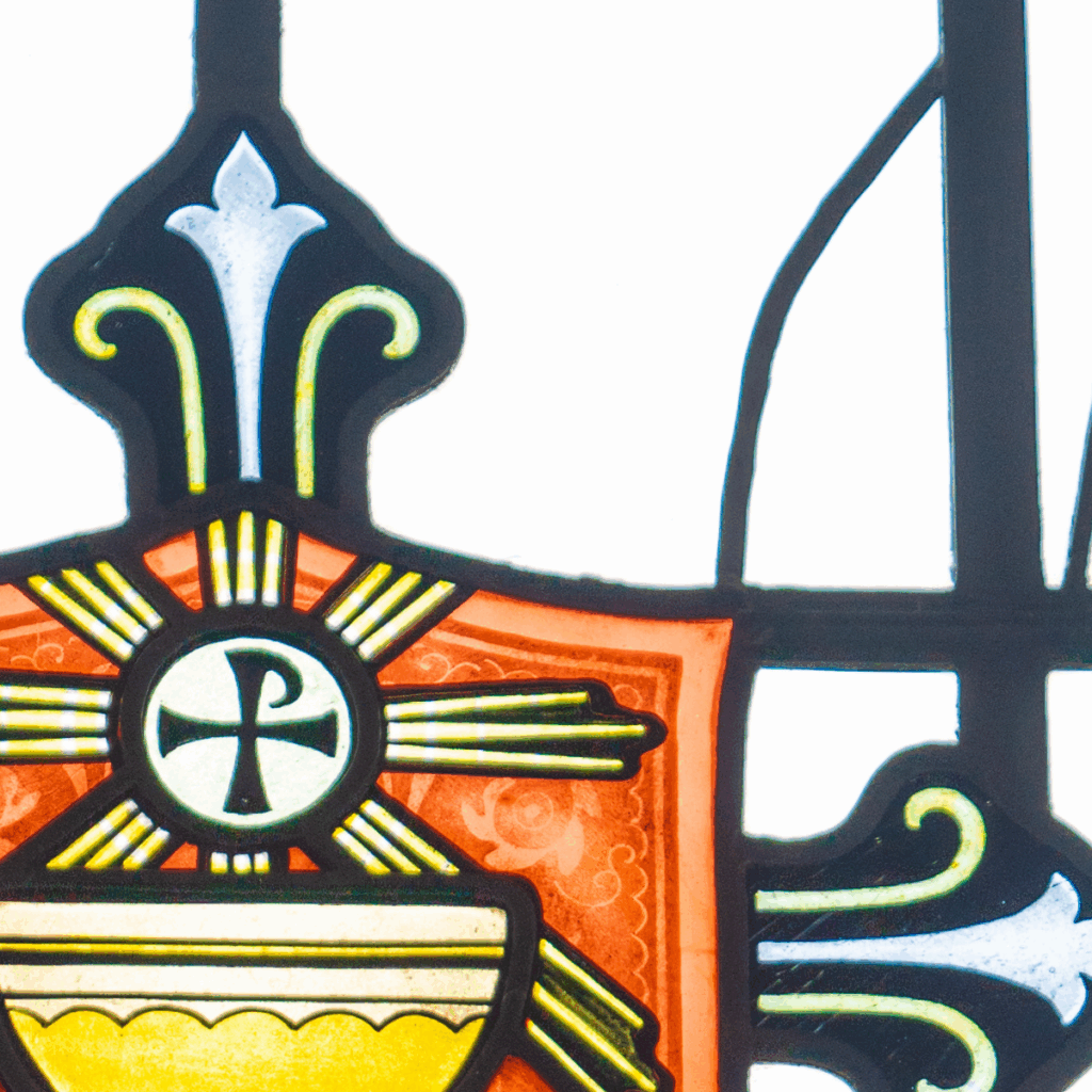Stained glass window featuring a central Chi Rho Christian symbol in a circle, yellow and orange geometric patterns, and decorative black outlines on a white background.