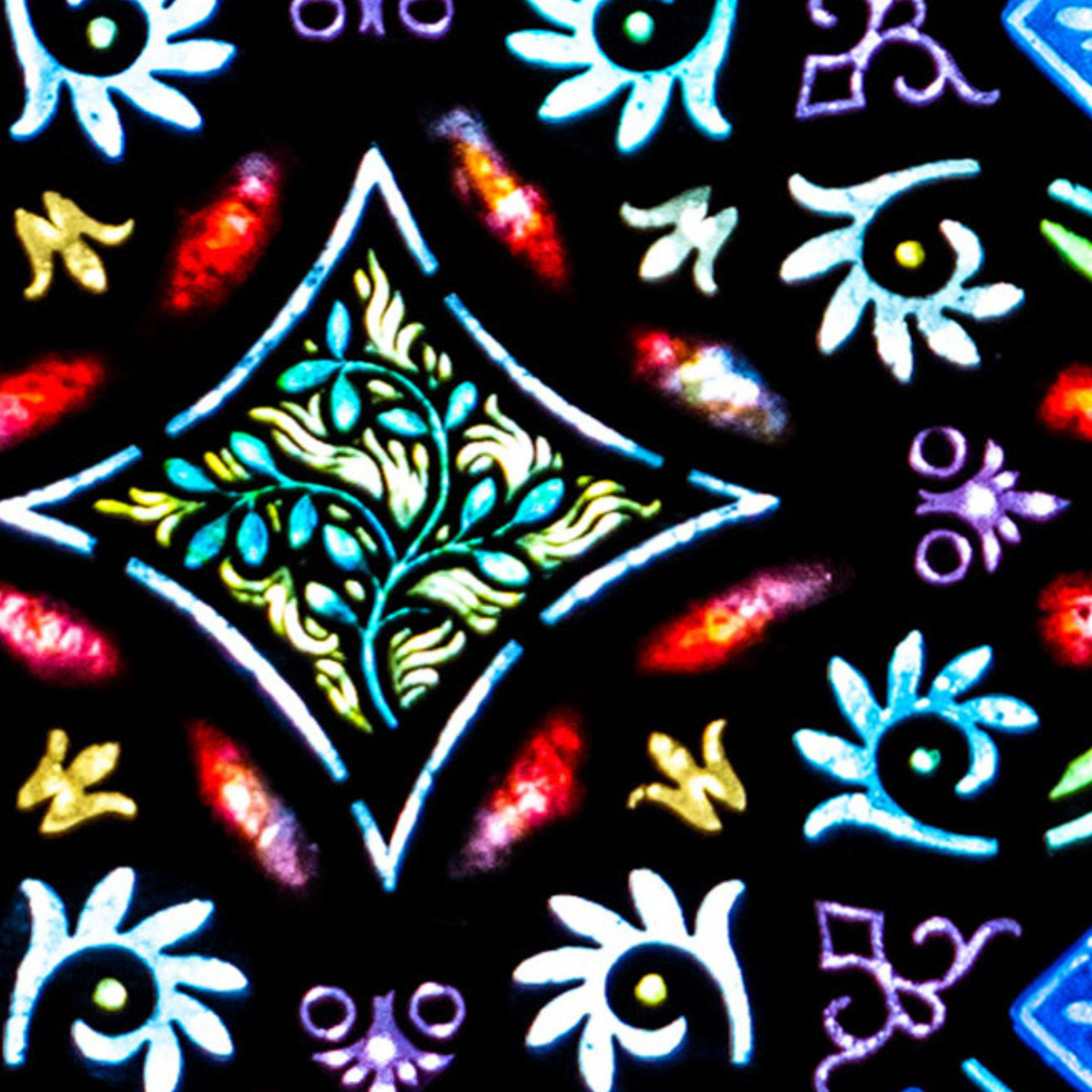 Colorful stained glass pattern featuring a central green leafy diamond shape, surrounded by white, blue, red, and yellow floral and geometric designs on a black background.