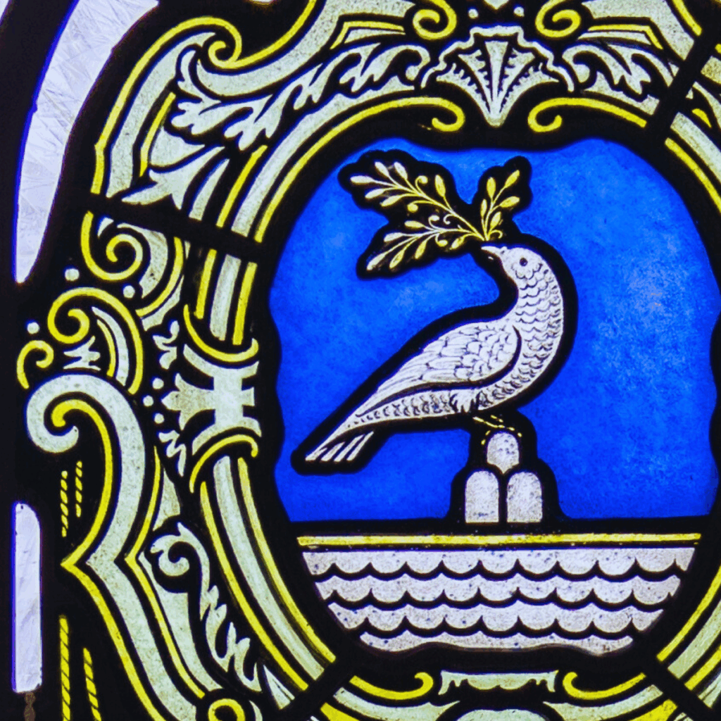 A stained glass window depicts a white dove holding an olive branch, perched on a fountain, with ornate yellow and black decorative patterns framing a bright blue background.