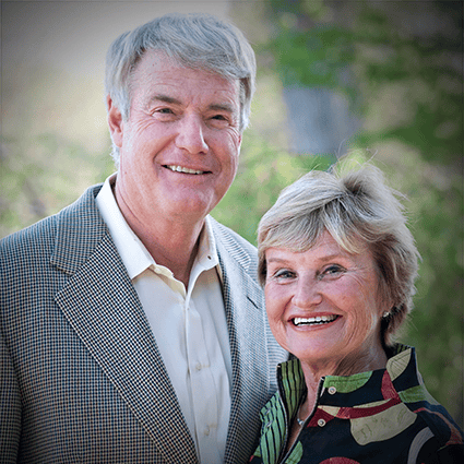 An older couple, a man in a gray checkered blazer and a woman in a colorful blouse, smile at the camera. Below them is a testimonial about their support for Saint John's School of Theology and Seminary, signed -Dan and Lynn Fazendin.