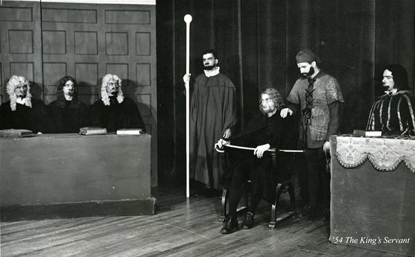 A black and white scene depicting a historical court setting. Four men in wigs sit behind a bench on the left. In the center, a man in robes holds a staff. Another man is seated with a bow, and two others stand beside him. A caption reads: "154 The King's Servant".