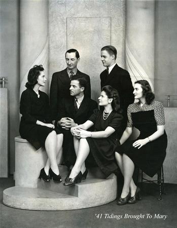 A vintage black and white photo of six people in formal attire from the 1940s. Three men are standing, and three women are seated. The backdrop is simple with soft lighting. In the bottom corner, it reads "'41 Tidings Brought To Mary.