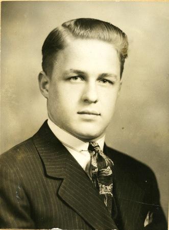 Vintage black and white portrait of a young man in a suit and tie with a neatly combed hairstyle, posing against a plain background.
