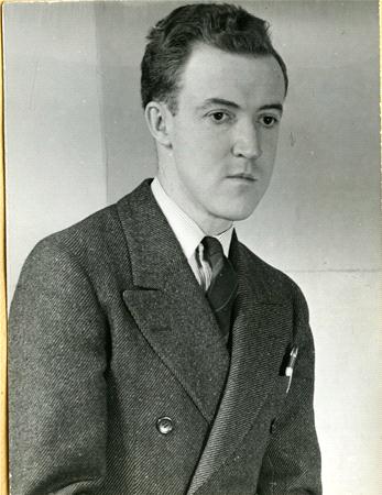 Black and white photo of a man in a double-breasted suit with a tie, sitting against a plain background. His hair is neatly combed, and he appears to be looking off to the side.