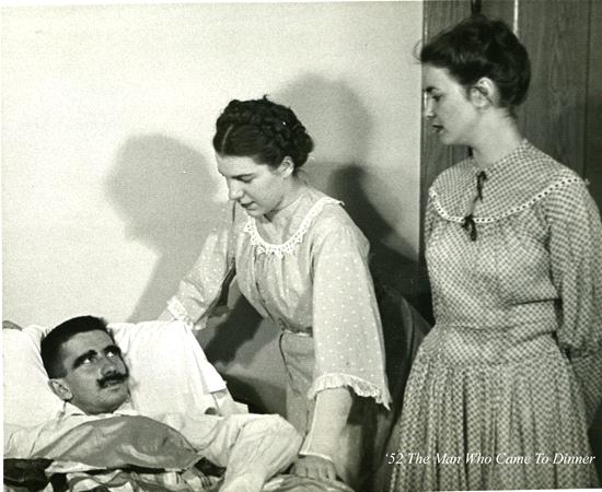 A black and white scene shows two women in 1950s-style dresses standing next to a mustached man lying in a bed. One woman leans over, touching his shoulder, while the other stands beside them. Text in the image reads, “The Man Who Came to Dinner.”.