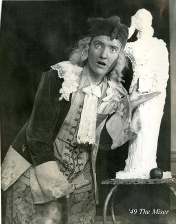 A person in 18th-century attire, including a tricorn hat and ruffled clothing, poses dramatically next to a plaster statue. The caption reads "'49 The Miser." The scene suggests a theatrical performance.
