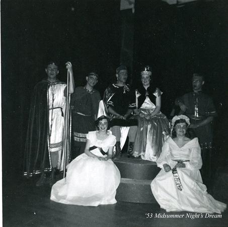 A black and white photo of a theater group in costumes on stage. Two people are seated on a platform while others stand and kneel around them, wearing robes and gowns. A handwritten note reads, "'53 Midsummer Night's Dream.