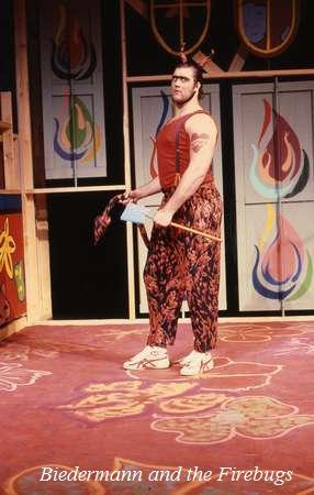 A person stands on a colorful stage holding an axe. They wear a sleeveless top, patterned pants, and sneakers. The backdrop features abstract, flame-like designs. Text at the bottom reads "Biedermann and the Firebugs.